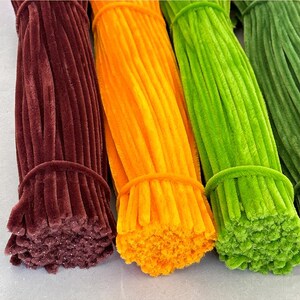 May include: Three bundles of pipe cleaners in different colors: brown, orange, and green. The pipe cleaners are bundled together and ready to be used for crafts.