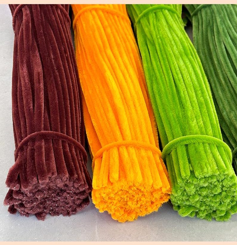 May include: Three bundles of pipe cleaners in different colors: brown, orange, and green. The pipe cleaners are bundled together and ready to be used for crafts.