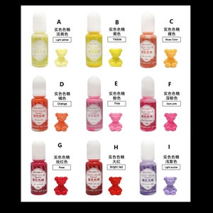 K&ouml;nnte beinhalten: Neun kleine Flaschen mit Harzpigment in verschiedenen Farben, darunter Hellgelb, Gelb, Nude, Orange, Rosa, Dunkelrosa, Rose, Rot und Helllila. Jede Flasche hat eine kleine B&auml;renfigur in der entsprechenden Farbe.