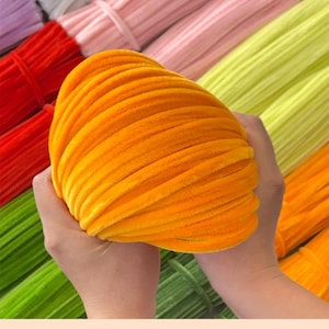 May include: A close-up of a bright orange velvet pipe cleaner. The pipe cleaner is soft and fluffy, and it is perfect for crafting projects.
