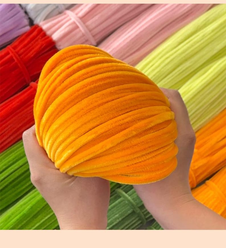 May include: A close-up of a bright orange velvet pipe cleaner. The pipe cleaner is soft and fluffy, and it is perfect for crafting projects.