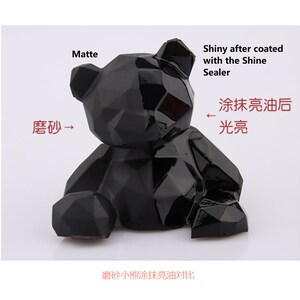 May include: A black geometric bear figurine, shown in two states: matte and shiny after being coated with a sealant. The text "Matte" is above the matte bear, and the text "Shiny after coated with the Shine Sealer" is above the shiny bear. The text "磨砂" is next to the matte bear, and the text "涂抹亮油后光亮" is next to the shiny bear. The text "磨砂小熊涂抹亮油对比" is below the bears.