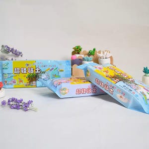 Può includere: Sono esposti diversi pacchetti di Super Clay, ciascuno in un involucro azzurro e giallo. La confezione presenta illustrazioni colorate e caratteri cinesi. L'argilla è probabilmente destinata a lavori manuali e progetti artistici per bambini.