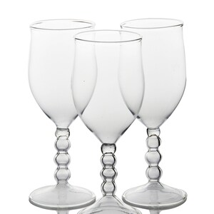 May include: Three clear wine glasses with a bulbous stem design. The glasses have a tulip-shaped bowl and a wide base. The stems feature a series of rounded glass beads. The glasses are transparent and reflect light.