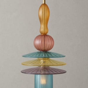 May include: A colorful pendant light fixture with a stacked design. The light features a series of glass elements in shades of amber, pink, teal, yellow, and purple. The bottom element is a blue cylindrical shape, and the light is suspended from a black cord.