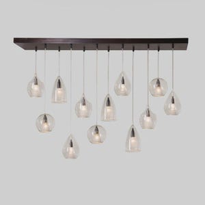 May include: A modern chandelier with a dark brown rectangular base, featuring 12 clear glass pendant lights of various shapes. Each pendant houses a single light bulb, creating a warm, inviting glow. The design is sleek and contemporary.