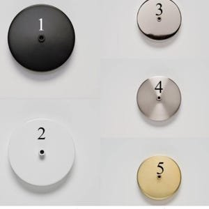May include: A collection of five circular metal ceiling canopy plates in various finishes: black, white, brushed nickel, stainless steel, and brass. Each plate has a central hole and is labeled with a number from 1 to 5.