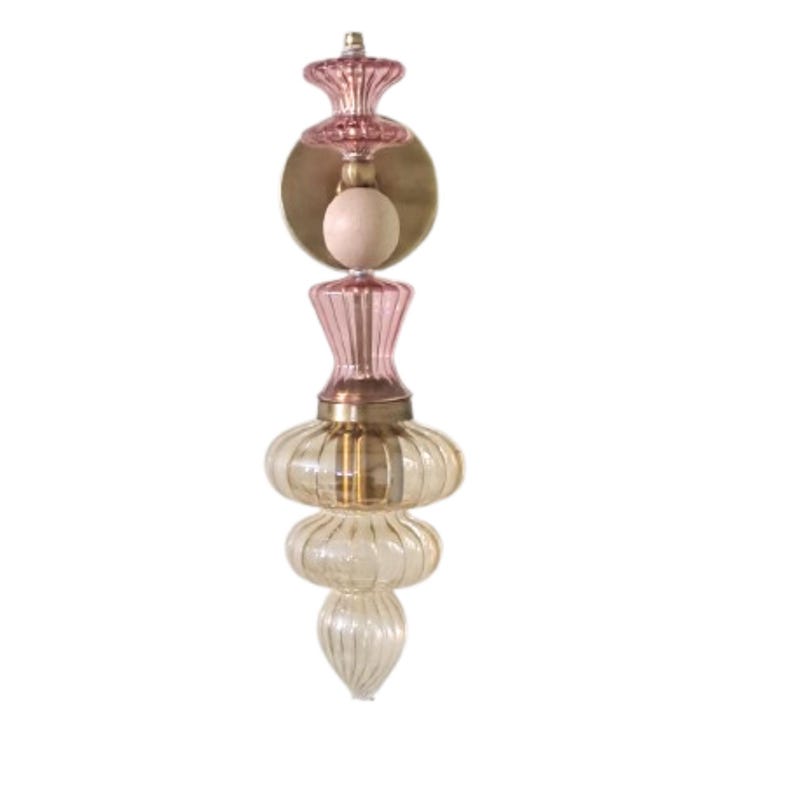 May include: A decorative wall sconce with a layered design. The sconce features a combination of pink and clear glass elements, brass accents, and a light bulb. The overall design is elegant and vintage-inspired.