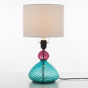 Puede incluir: Una lámpara de mesa decorativa con una base de cristal turquesa y rosa y una pantalla de color crema. La base tiene un diseño único en espiral. La lámpara mide aproximadamente 51 cm de altura.