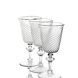 May include: Three clear wine glasses with a spiral design on the bowl. The glasses have a decorative stem and a round base. The glasses are made of glass and are set against a white background.