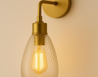 May include: A gold-toned wall sconce with a clear, teardrop-shaped glass shade featuring a spiral design. The light fixture includes a vintage-style bulb and a circular wall mount. The overall design is elegant and suitable for interior lighting.