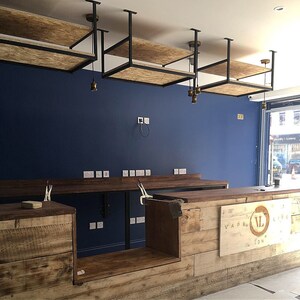 Puede incluir: Interior de un local comercial en construcci&oacute;n. Presenta una pared azul oscuro, estanter&iacute;as de madera y un mostrador con el texto "Vape Life London". El dise&ntilde;o incorpora madera vista y detalles en metal negro.