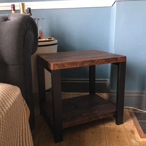 May include: A small, square side table with a dark stained wooden top and a lower shelf. The legs and frame are black. The table is approximately 20 inches tall and 20 inches wide.
