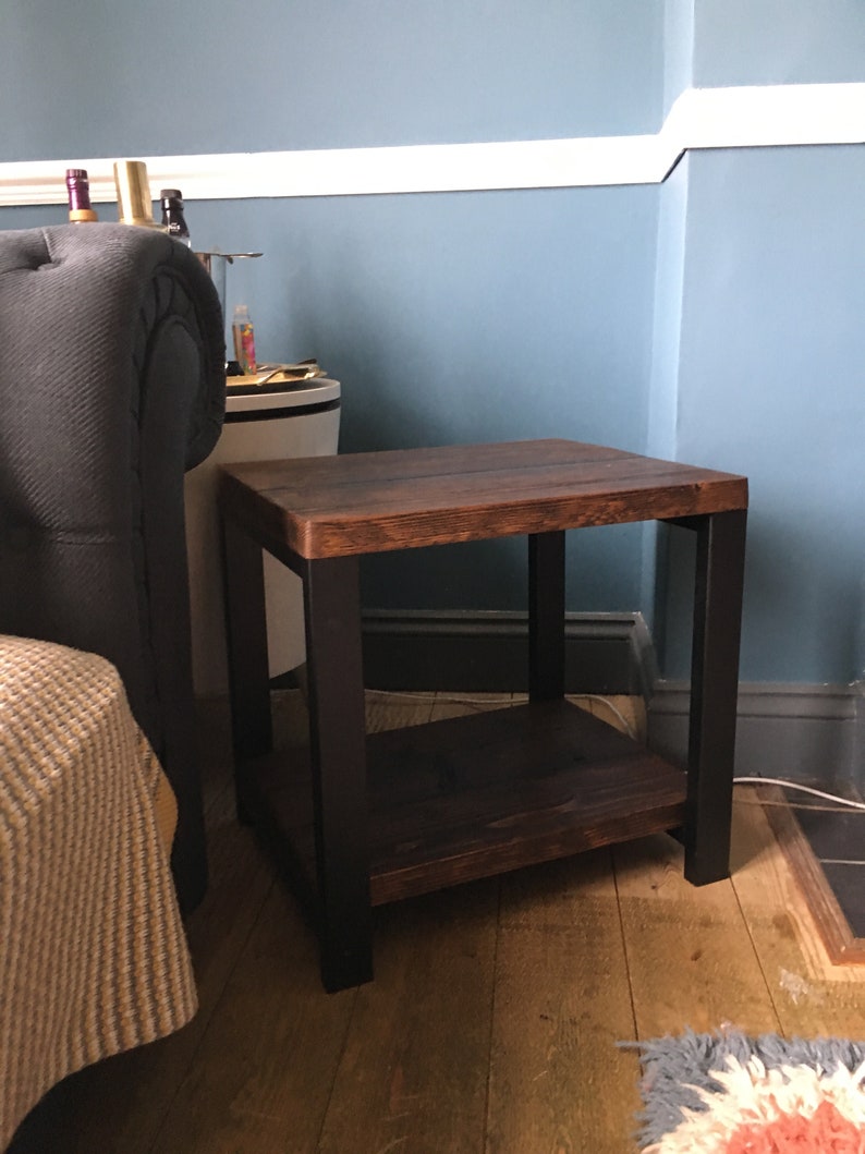 May include: A small, square side table with a dark stained wooden top and a lower shelf. The legs and frame are black. The table is approximately 20 inches tall and 20 inches wide.