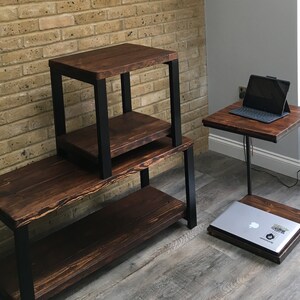 May include: Set of three dark brown wooden tables with black metal frames. One is a long, low table with a shelf, another is a two-tiered side table, and the third is a C-shaped table with a laptop on top.