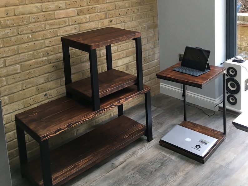 May include: Set of three dark brown wooden tables with black metal frames. One is a long, low table with a shelf, another is a two-tiered side table, and the third is a C-shaped table with a laptop on top.