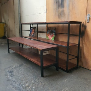 May include: Two wooden shelves with a dark finish and black metal frames. The shelves are rectangular and have multiple levels for storage. One is a low, long bench, and the other is a taller, wider unit. Books are displayed on the shelves.