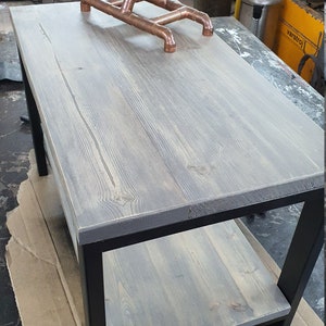 May include: A gray wooden coffee table with a black metal frame and a lower shelf. A copper pipe lamp with a large bulb sits on the table. The table is approximately 48 inches long and 24 inches wide.