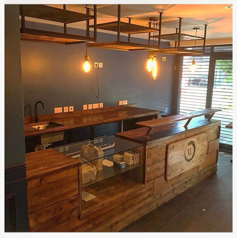 Puede incluir: Vista interior de un espacio comercial con dise&ntilde;o r&uacute;stico. Cuenta con encimeras de madera, estanter&iacute;as y un mostrador con vitrina de cristal. L&aacute;mparas colgantes con bombillas Edison iluminan la zona. Las paredes est&aacute;n pintadas de azul oscuro.