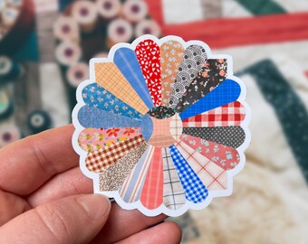 May include: A colorful patchwork flower sticker with a variety of patterns and colors, including red, blue, yellow, and brown.