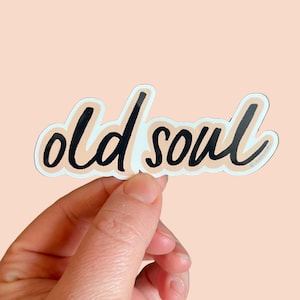 May include: A sticker with the words "old soul" written in black cursive script on a peach background.