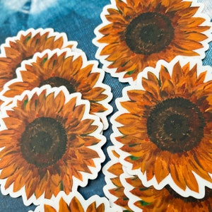 Peut inclure: Plusieurs autocollants repr&eacute;sentant des tournesols. Chaque autocollant pr&eacute;sente une peinture &agrave; l'aquarelle d&eacute;taill&eacute;e d'un tournesol avec des p&eacute;tales orange et un centre brun fonc&eacute;. Les autocollants ont une bordure blanche.