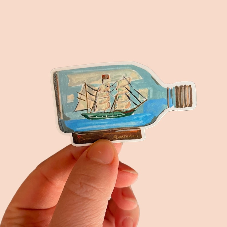 May include: A sticker of a ship in a bottle. The bottle is clear glass with a blue liquid inside. The ship is a small wooden sailboat with white sails. The sticker has a white background and the text "@LAURENSPIRED" at the bottom.