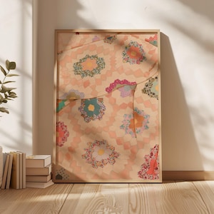 Pode incluir: Impressão emoldurada com um design detalhado de colcha. A colcha apresenta um padrão floral repetido sobre um fundo pêssego, com motivos florais coloridos. A moldura é de madeira clara e a impressão está encostada a uma parede branca.