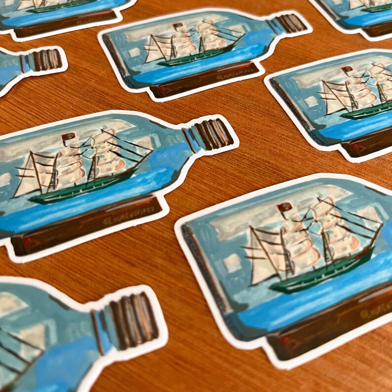 May include: A set of stickers featuring a ship in a bottle. The bottle is clear glass with a blue liquid inside. The ship is white with brown sails and a black flag. The stickers are printed on white paper with a white border.
