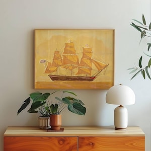 Könnte beinhalten: Gerahmtes Gemälde eines Dreimast-Segelschiffs mit gelben Segeln und einem braunen Rumpf. Das Kunstwerk ist vor einem gelben Hintergrund platziert und zeigt eine amerikanische Flagge. Das Gemälde wird über einem Holzschrank mit Pflanzen und einer weißen Lampe ausgestellt.