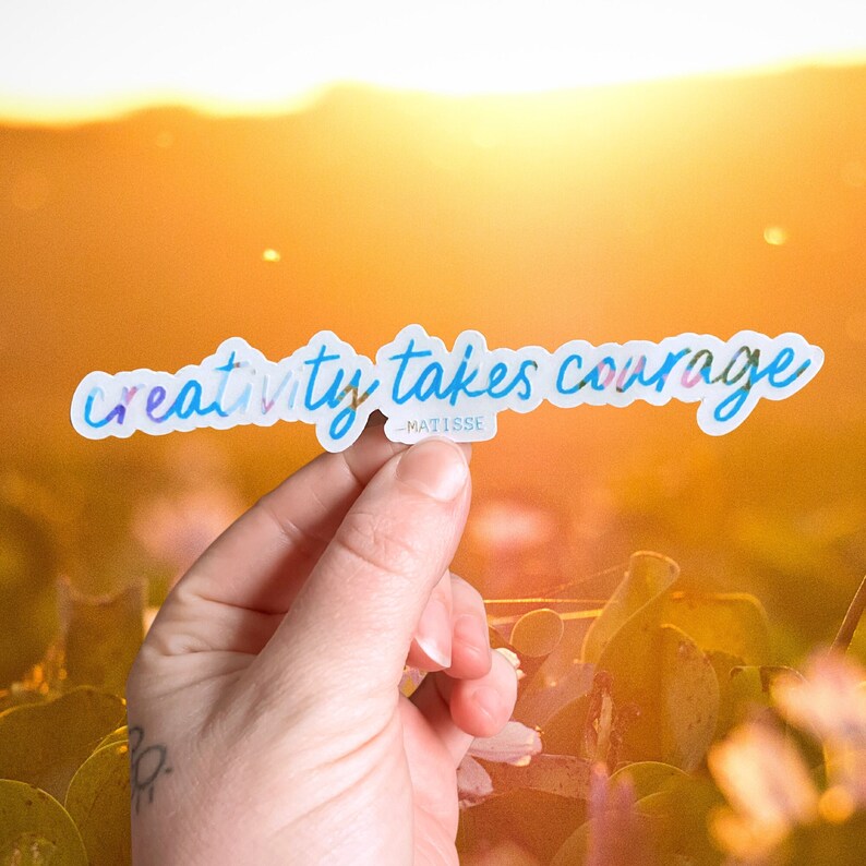 K&ouml;nnte beinhalten: Ein Aufkleber mit dem Text "creativity takes courage" in einer blauen und pinken Farbverlaufschrift. Der Text wird Matisse zugeschrieben.