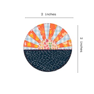 May include: A 2-inch diameter round fabric patch with a patchwork design of a sunset over a wavy ocean. The sunset is made of orange, blue, and white fabric with a floral pattern in the center. The ocean is a dark blue fabric with white stitching.
