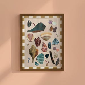 Op de afbeelding: Een ingelijst kunstwerk met een verzameling verschillende schelpen in tinten bruin, blauw, roze en wit. De schelpen zijn gerangschikt op een beige achtergrond met een goud-wit gestreepte rand, omlijst door een bruine houten lijst.
