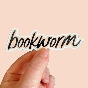 May include: A black and white sticker with the word "bookworm" written in a cursive font. The sticker is on a peach background.