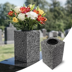 Peut inclure: Un vase rectangulaire en granit avec une finition mouchetée grise et noire. Le vase présente un insert circulaire en plastique noir sur le dessus pour maintenir des compositions florales. Une vue montre le vase rempli de fleurs blanches, jaunes et rouges.