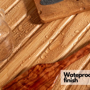 May include: Close-up of a wooden cutting board, a wooden spatula, and a glass object on a bamboo surface. The bamboo surface has a waterproof finish and is covered in water droplets. The text "Waterproof finish" is visible.