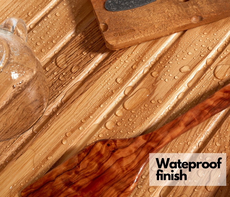 May include: Close-up of a wooden cutting board, a wooden spatula, and a glass object on a bamboo surface. The bamboo surface has a waterproof finish and is covered in water droplets. The text "Waterproof finish" is visible.
