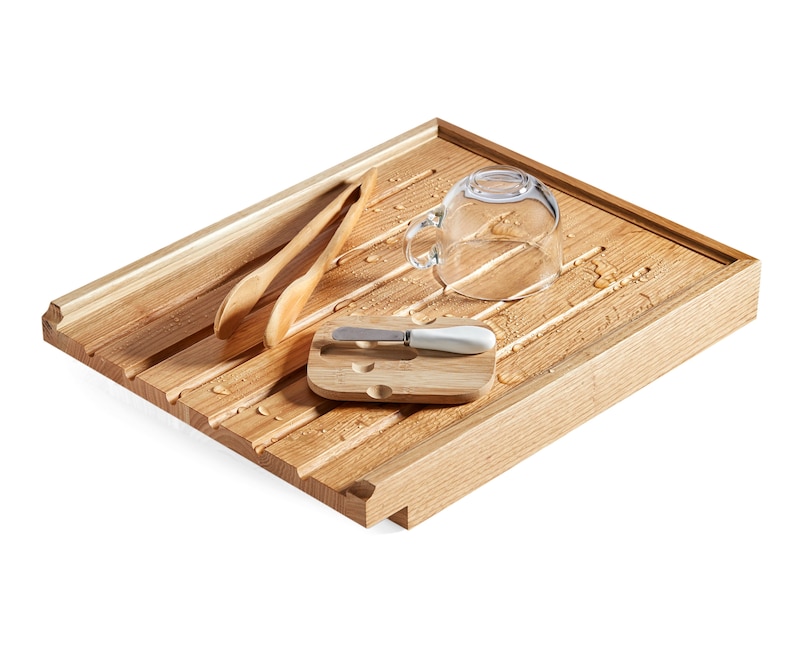 May include: A wooden dish drying rack with a rectangular shape and grooved surface. It holds two wooden spoons, a small bamboo cutting board with a butter knife, and a clear glass teacup. Water droplets are visible on the rack.