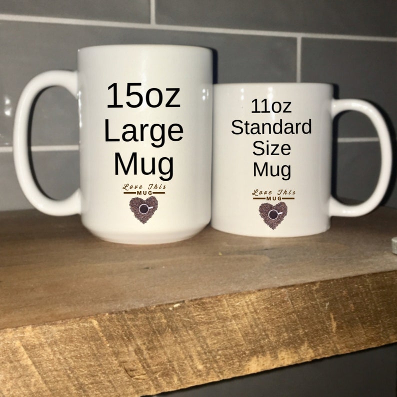 May include: Two white ceramic mugs with black text and a coffee bean heart design. The larger mug is labeled "15oz Large Mug" and the smaller mug is labeled "11oz Standard Size Mug".