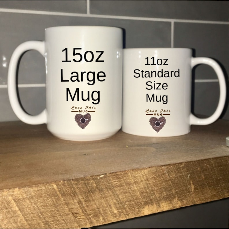 May include: Two white ceramic mugs with black text and a brown coffee bean heart design. The larger mug is 15oz and says "Large Mug". The smaller mug is 11oz and says "Standard Size Mug".