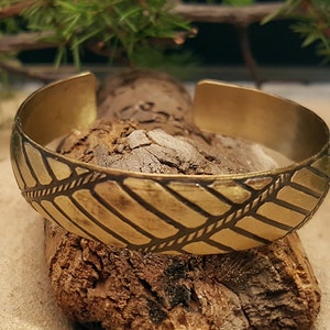Könnte beinhalten: Ein goldfarbenes Metallarmband mit geometrischem Muster. Das Armband ist breit und hat eine leicht gebogene Form.