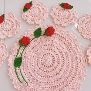 Puede incluir: Juego de seis manteles individuales de crochet rosa con delicados diseños florales. Cada mantel individual presenta una rosa de crochet con hojas verdes en el centro.