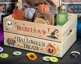 Op de afbeelding: Houten Halloween-cadeaukrat met de tekst "ISABELLA'S" en "HALLOWEEN TREATS". De krat bevat pompoenvormige kaarsen, kleine flesjes en een doos met het opschrift "Fun Autumnal Craft". Halloween-decoraties zijn aanwezig.