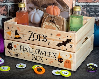 Może przedstawiać: Drewniany zestaw pudełek na Halloween z napisem "ZOE'S HALLOWEEN BOX" i świątecznymi ilustracjami. Pudełko zawiera świece w kształcie dyni, butelki i zestaw rzemieślniczy. Rozrzucone są dekoracyjne konfetti o tematyce Halloween.