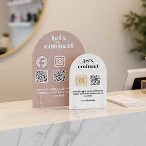 May include: Two arched signs with the text "Let's connect" and social media icons. One sign is pink with the Facebook and Instagram logos and QR codes. The other is white with a QR code and a gold circle.