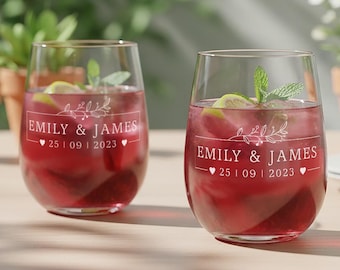 May include: Two clear stemless wine glasses filled with a dark red liquid, ice cubes, and a lime wedge garnish. Each glass features white printed text reading EMILY & JAMES, the date 25 | 09 | 2023, a small floral branch graphic, and two hearts.