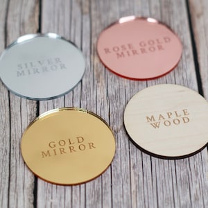 May include: Four round coasters with different finishes. The coasters are made of wood, silver mirror, gold mirror, and rose gold mirror. The coasters have the following text: "Silver Mirror", "Gold Mirror", "Rose Gold Mirror", and "Maple Wood".