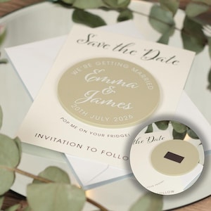 May include: Save the Date magnet with a beige background and white text. The magnet says "We're getting married Emma & James 20th July 2026". The magnet is attached to a white card that says "Save the Date" and "Pop me on your fridge, invitation to follow".