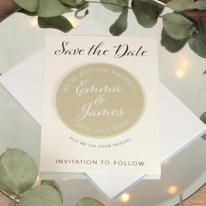 May include: Save the Date magnet with a beige circle featuring the text "We're getting married Emma & James 20th July 2026". The magnet is on a white card with the text "Save the Date" and "Invitation to follow".