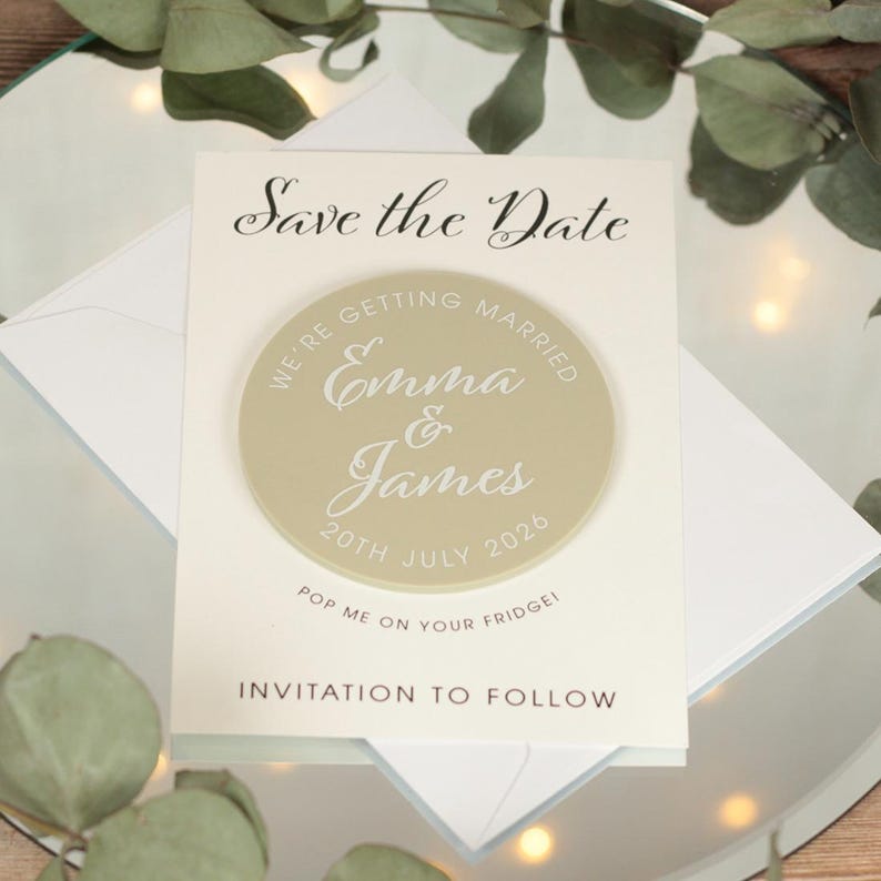 May include: Save the Date magnet with a beige circle featuring the text "We're getting married Emma & James 20th July 2026". The magnet is on a white card with the text "Save the Date" and "Invitation to follow".